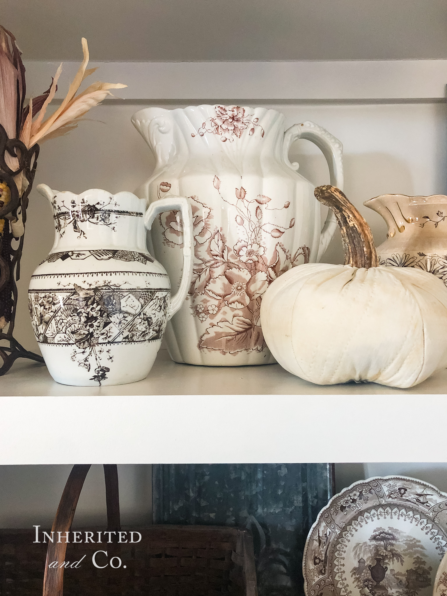 Large antique brown transferware pitcher in the background with a smaller brown transferware pitcher in the foreground and to the left with a quilted pumpkin on the right