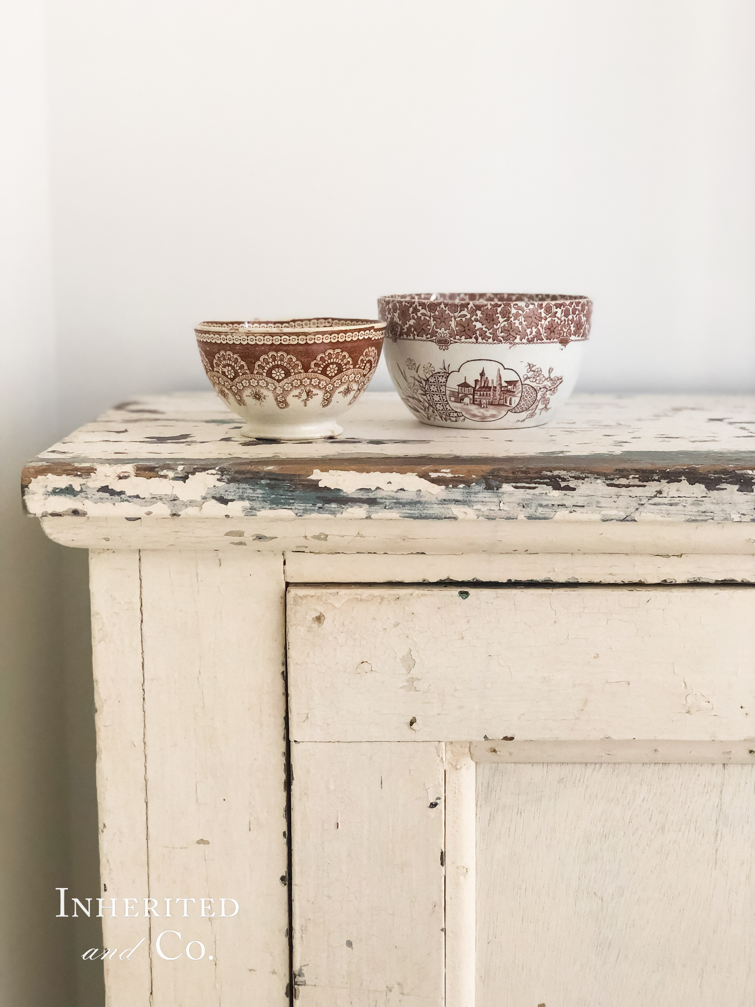 Corner of chippy white cabinet with two brown transferware bowls on top