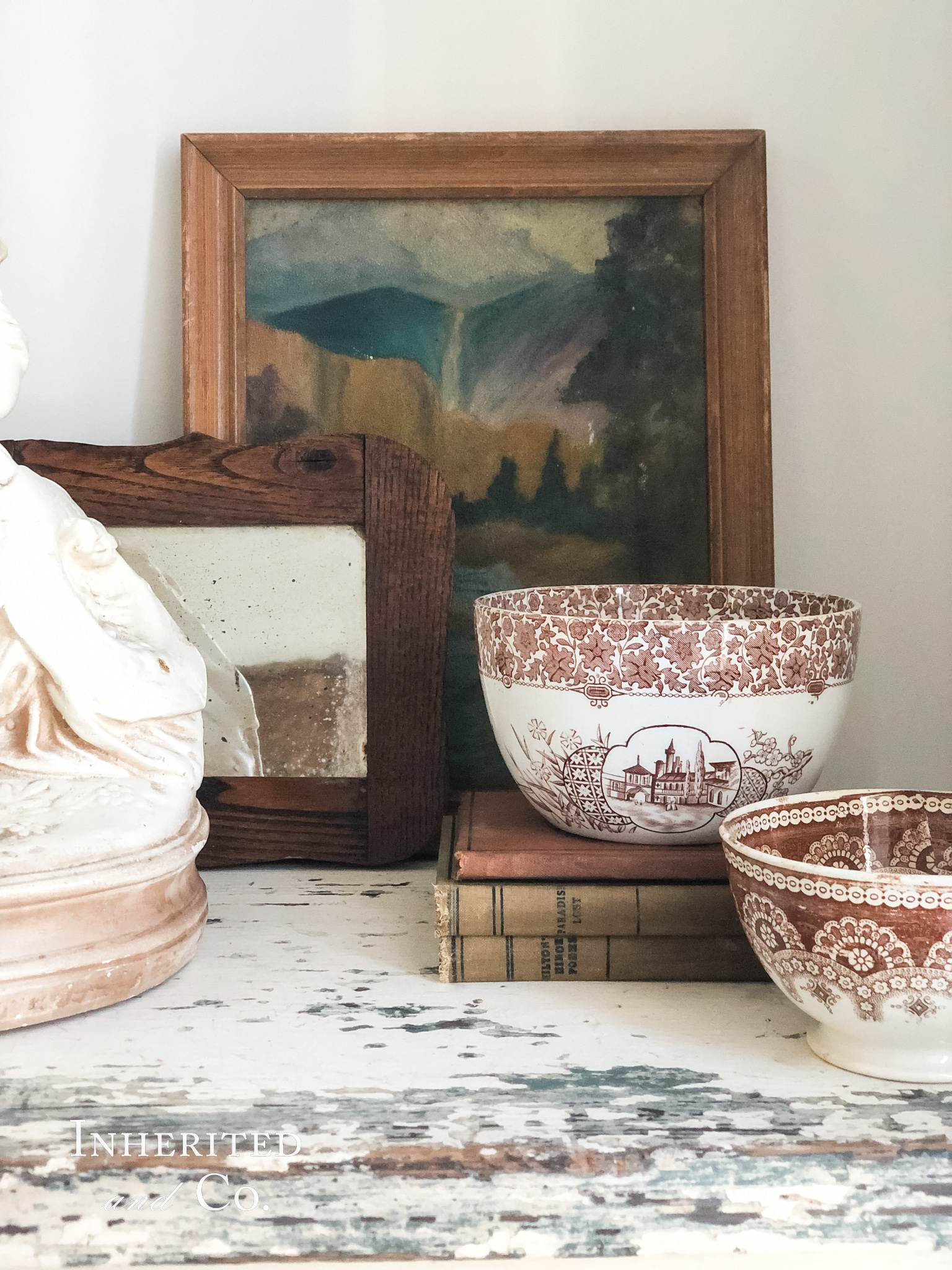 Antique vignette with a muted oil painting and small oak mirror in the background of two brown transferware bowls and a stack of books