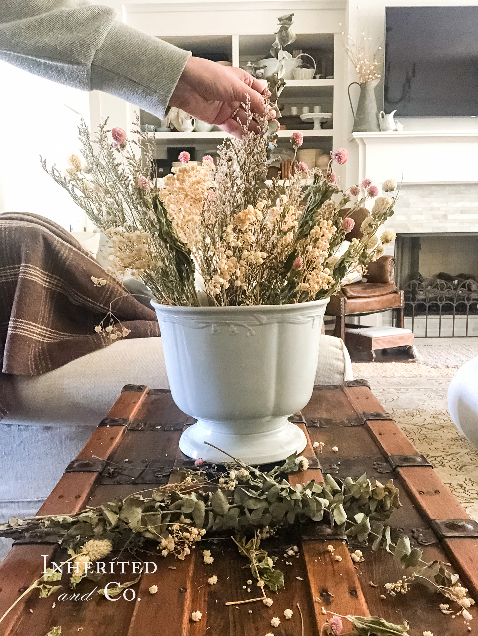 ironstone punch bowl filled with dried flowers sitting atop a steamer trunk with shelves of antiques in the background