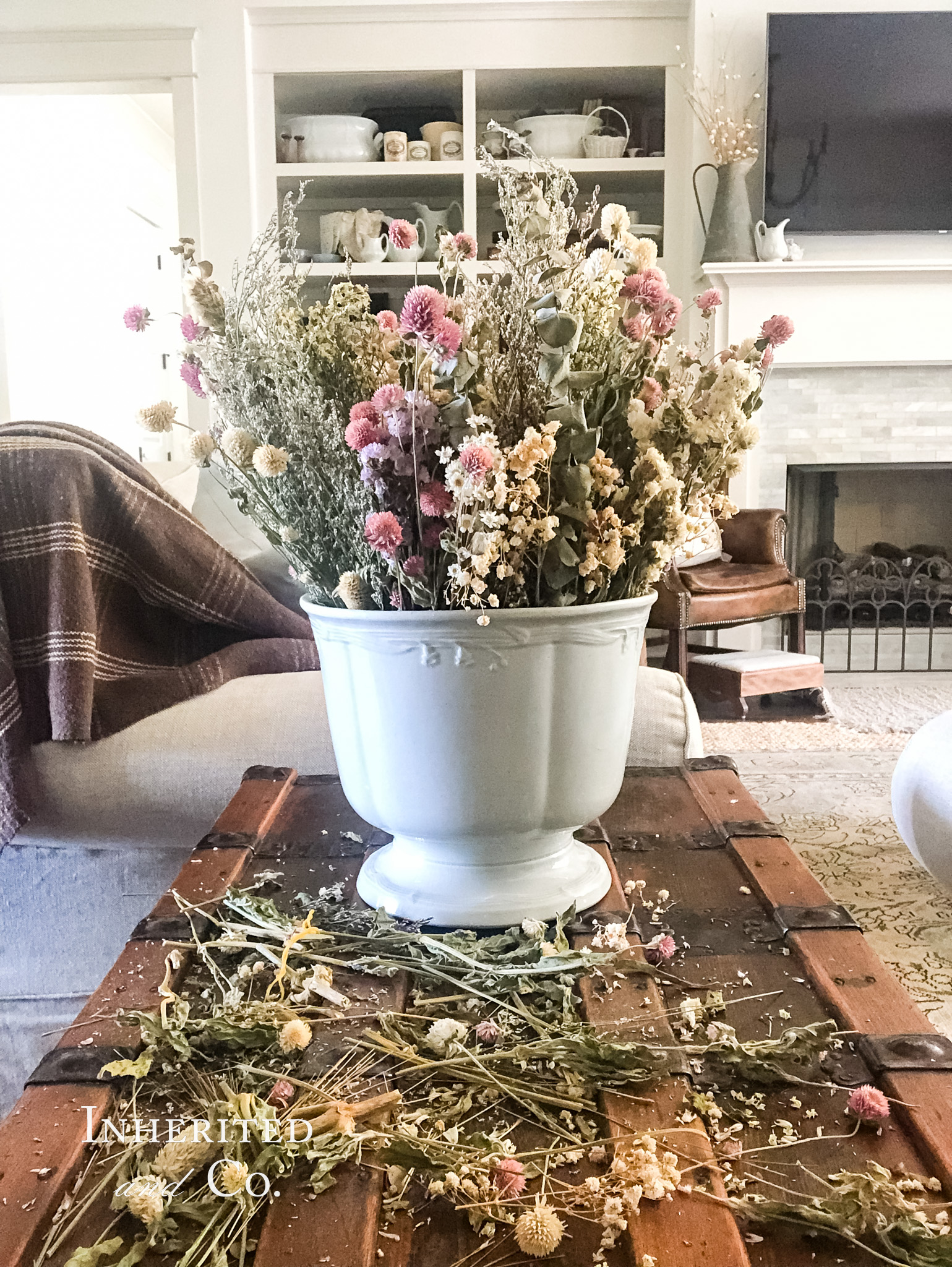 ironstone punch bowl filled with dried flowers sitting atop a steamer trunk with shelves of antiques in the background