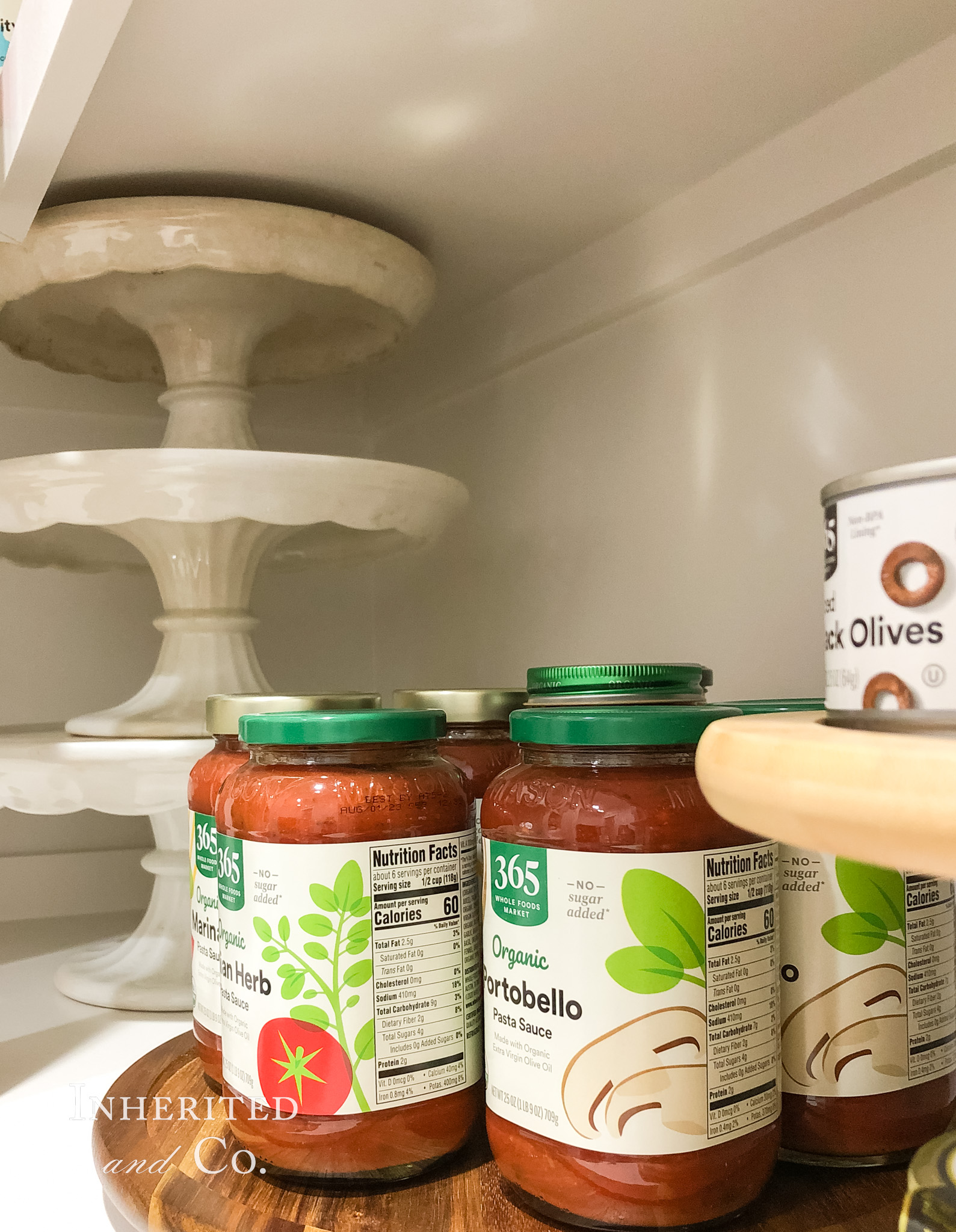 stack of antique ironstone cakestands and a lazy susan with pasta sauce on a pantry shelf