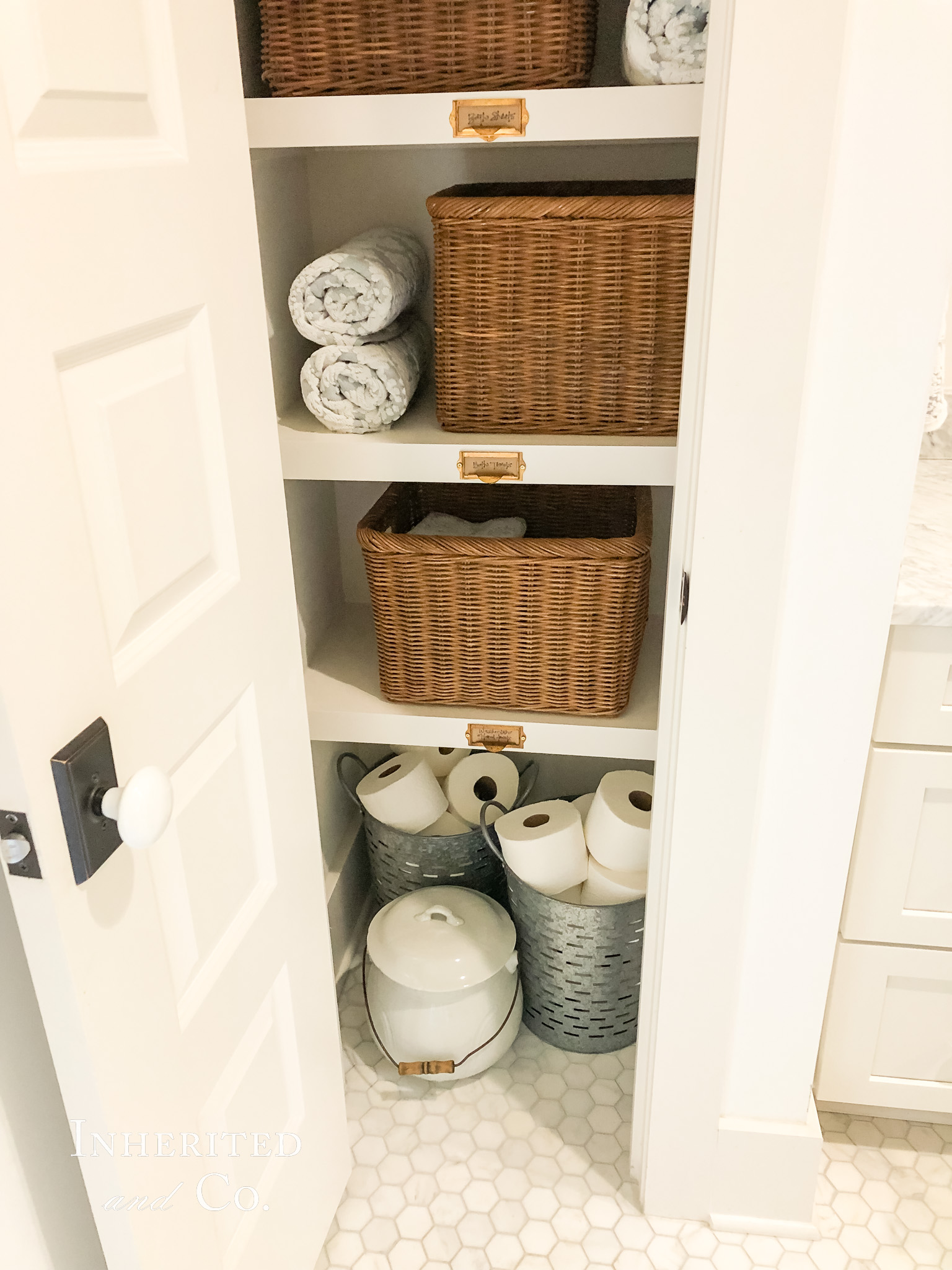 Bottom shelves, filled with baskets and ironstone, in an organized linen closet